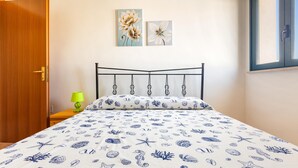 Un dormitorio con cama, una puerta de madera, una mesita de noche con lámpara y dos obras de arte en la pared.