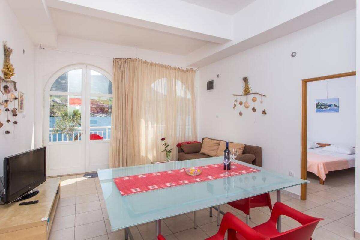 A modern living room with a glass dining table, red chairs, a sofa, and a TV.