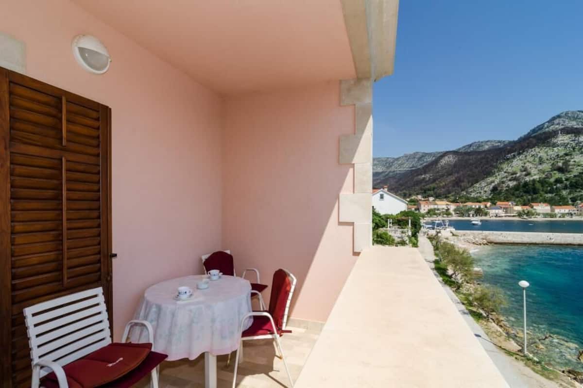 A balcony with a table and chairs, overlooking a coastal area with a mountain in the background.