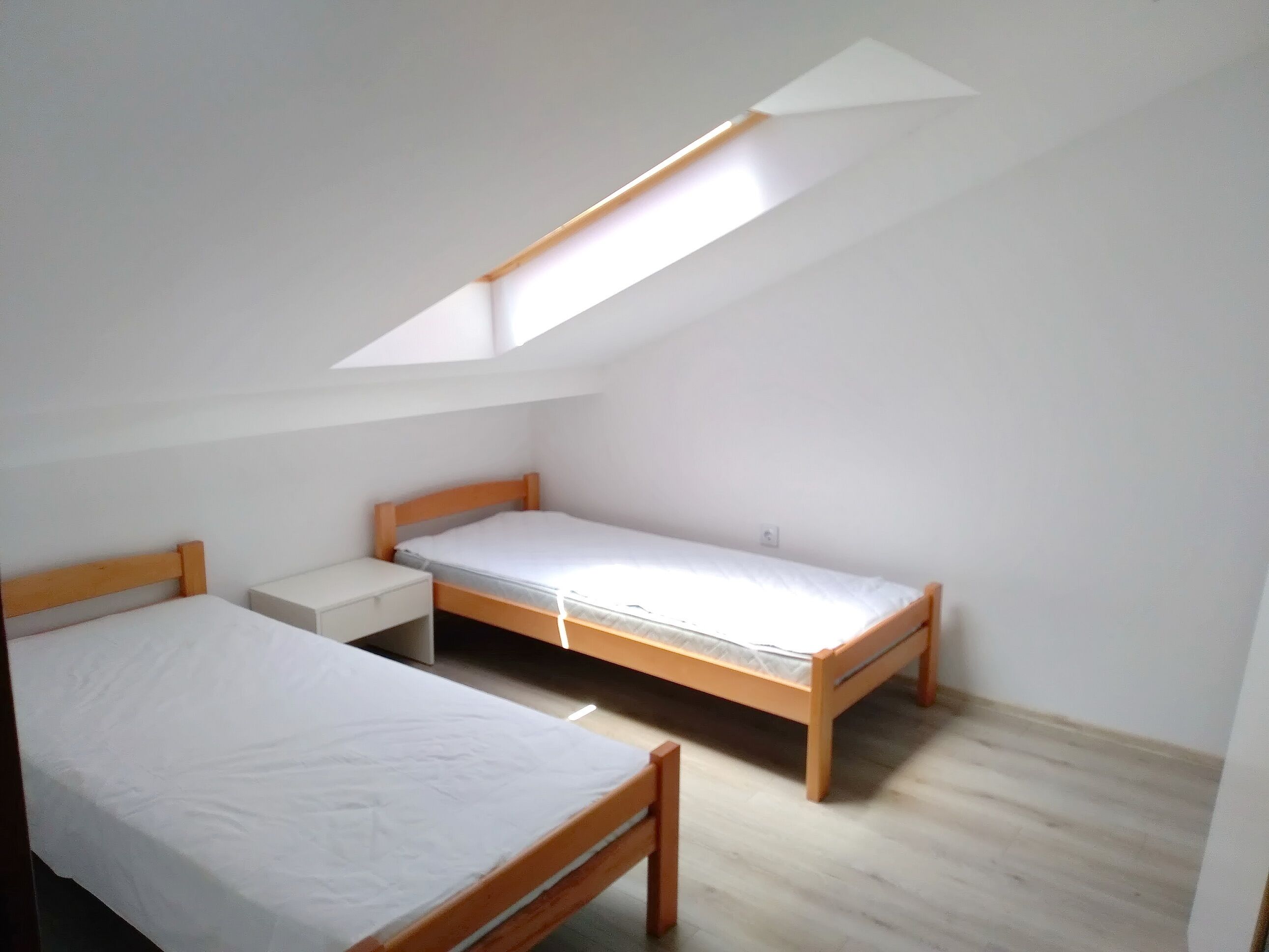 Ein kleiner, heller Raum mit zwei Holzbetten und einem Dachfenster.