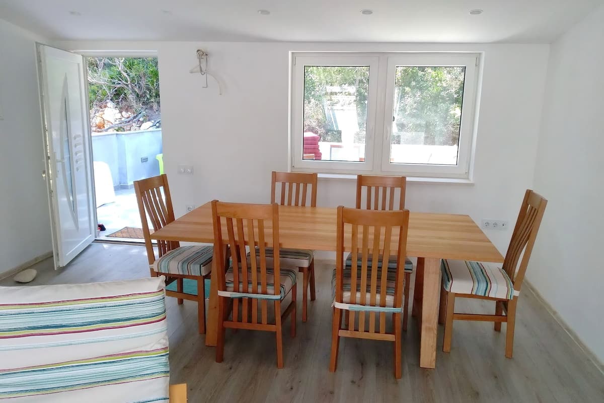 A dining area with a wooden table and six chairs, a striped sofa, and two windows providing natural light.