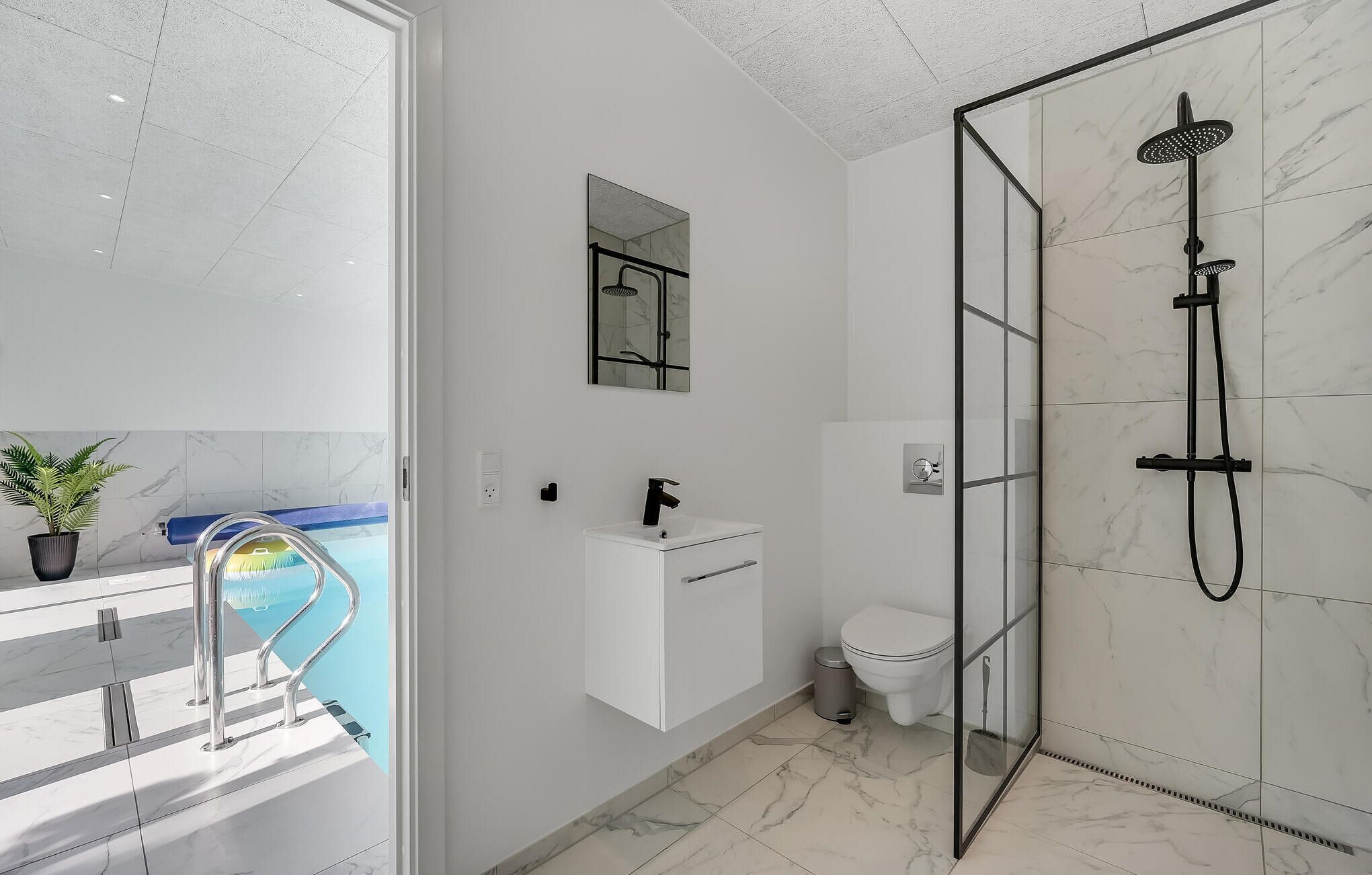 Een moderne badkamer met een douchecabine van glas, een wit wastafeltje en een toilet.