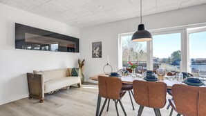 Ett modernt matområde med ett stort fönster, ett matbord dukat med blå tallrikar och en soffa med en dekorativ spegel ovanför.