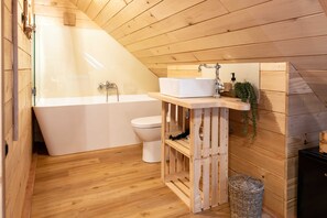 A wooden cabin bathroom with a bathtub, toilet, and wooden vanity with a sink and mirror.