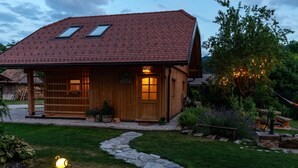 Eine Holzhütte mit geneigtem Dach, ein Steinweg, der zum Eingang führt, und ein gepflegter Garten mit verschiedenen Pflanzen und einer Bank.