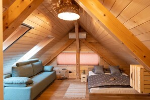 A cozy attic bedroom with a wooden ceiling, a sofa, a bed, and a small table.
