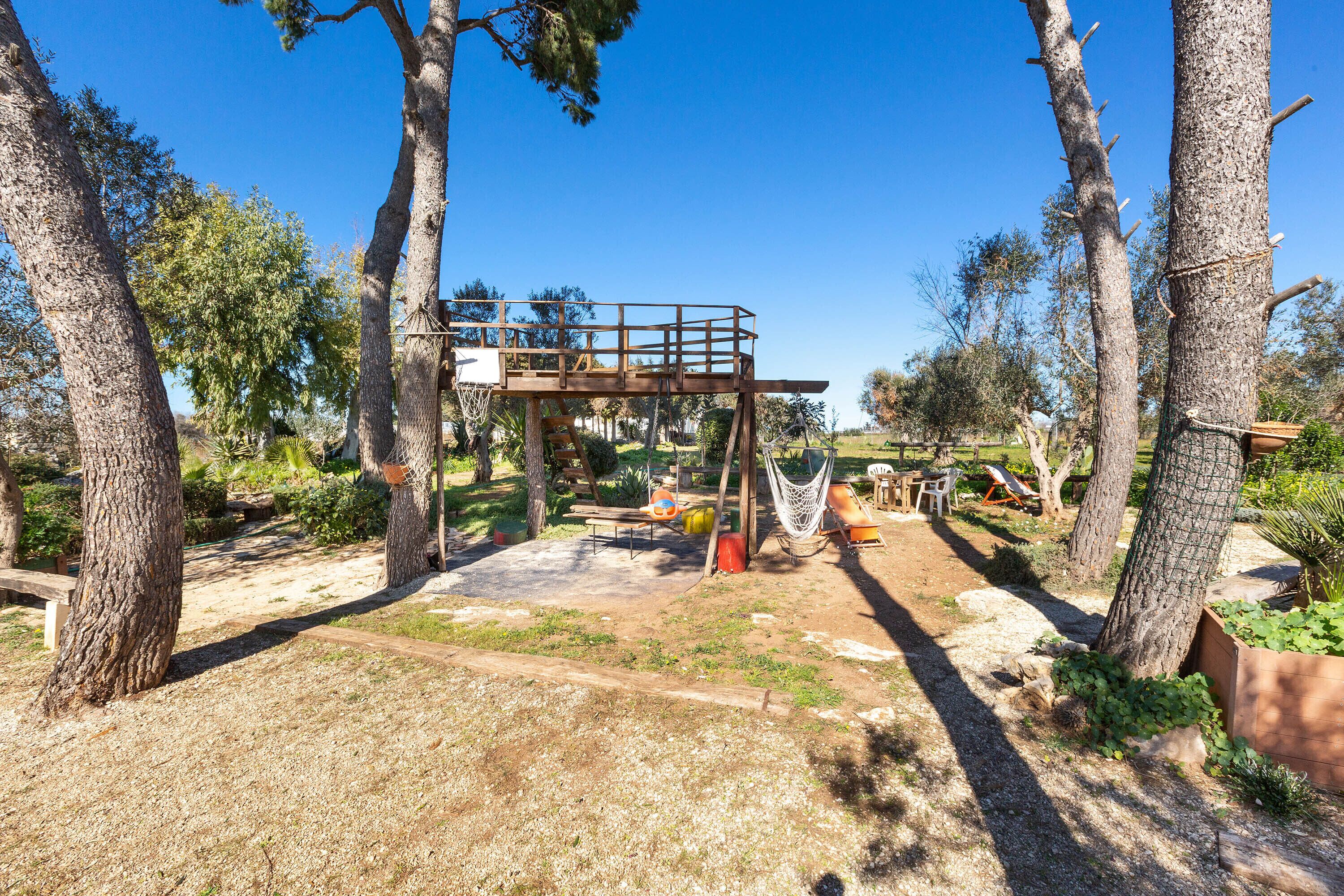 A wooden deck with a basketball hoop, surrounded by trees and a hammock.