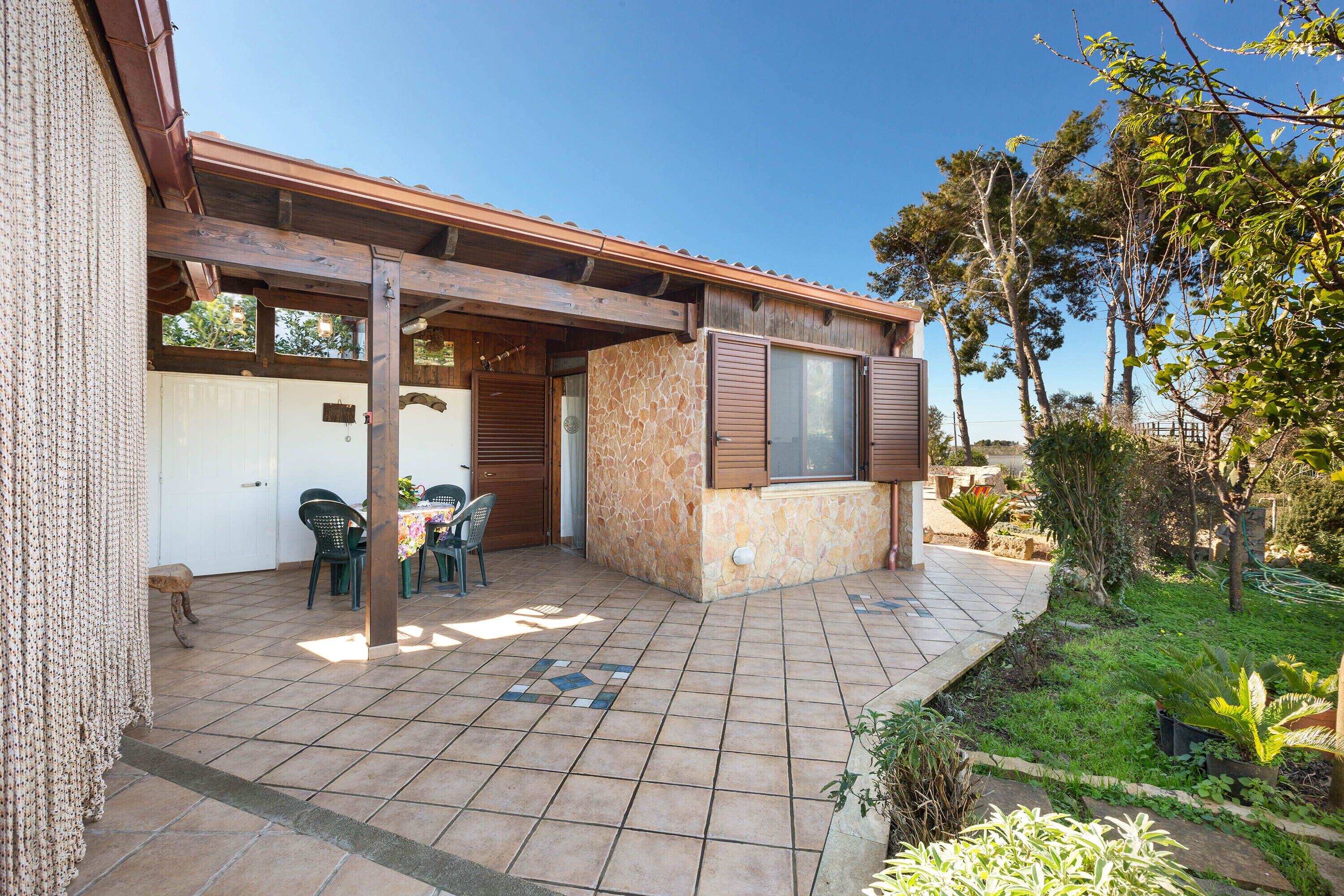 A patio with a table and chairs, a stone wall, and a wooden pergola.