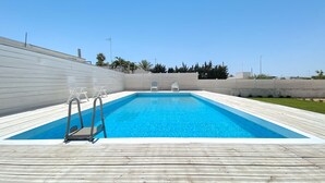 Ein rechteckiger Pool mit Holzterrasse, zwei Liegestühlen und einer Leiter.