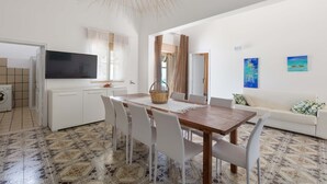 Eine moderne Küche mit weißen Schränken, einem großen Fernseher und einem Essbereich mit einem Holztisch und weißen Stühlen.