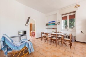 A dining area with a table and chairs, a television on a stand, and a window with blinds. - 2961 Villa Poesia by Barbarhouse (Porto Cesareo)