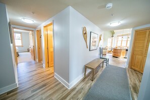 A spacious hallway with wooden flooring, a bench, and a rug leading to a kitchen area with wooden cabinets and a dining table. - Silver Mill 8244 (Keystone)