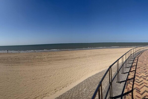 Ein Strand mit einem gepflasterten Weg und einer Geländer.