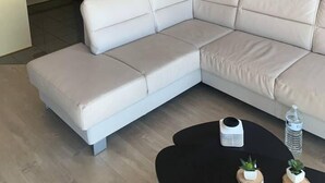A modern living room with a sectional sofa, a dining table, and a kitchen area in the background. - Beautiful 2-bed Apartment in Wenduine (De Haan)