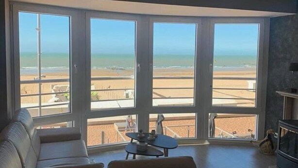 A living room with a large sliding glass door leading to a balcony with a view of the beach. - Beautiful 2-bed Apartment in Wenduine (De Haan)