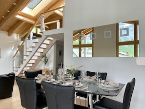 Ein Essbereich mit einem Tisch für vier Personen, einer Treppe und großen Fenstern mit Blick auf eine gebirgige Landschaft.