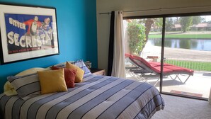 Une chambre à coucher avec un lit, des oreillers, un tableau encadré et une vue sur une piscine et un espace de détente extérieur.