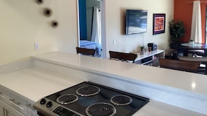Une cuisine moderne dotée d’un îlot central, un coin repas avec une table et des chaises, et un salon avec un téléviseur et des œuvres d’art.