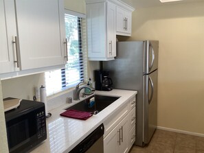 A kitchen with white cabinets, a stainless steel refrigerator, a coffee maker, and a microwave.