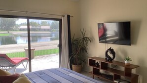 Une chambre à coucher avec un lit, une télévision, une plante et une vue sur un plan d’eau, visible à travers une porte coulissante.