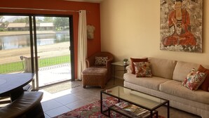 Un salon comprenant un canapé, un fauteuil et une table basse, un tableau accroché au mur et une vue sur une étendue d’eau, visible à travers une porte coulissante.