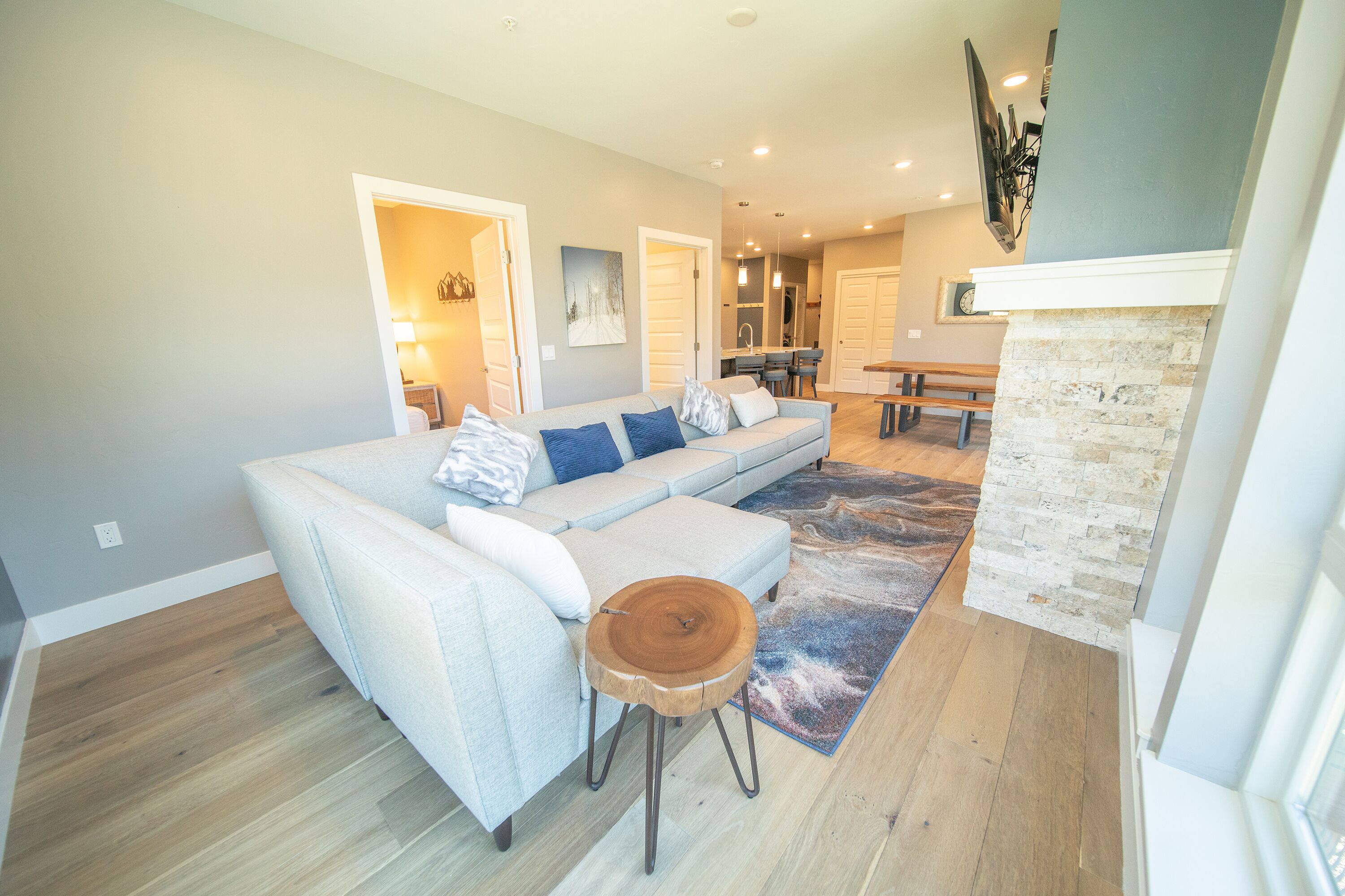 A modern living room with a sectional sofa, a round wooden stool, and a stone fireplace.