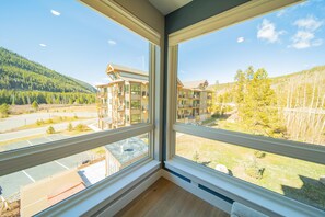 A room with large windows offering a view of a multi-story building and a forested hillside. - Clearwater Lofts Bldg 2 205 (Keystone)