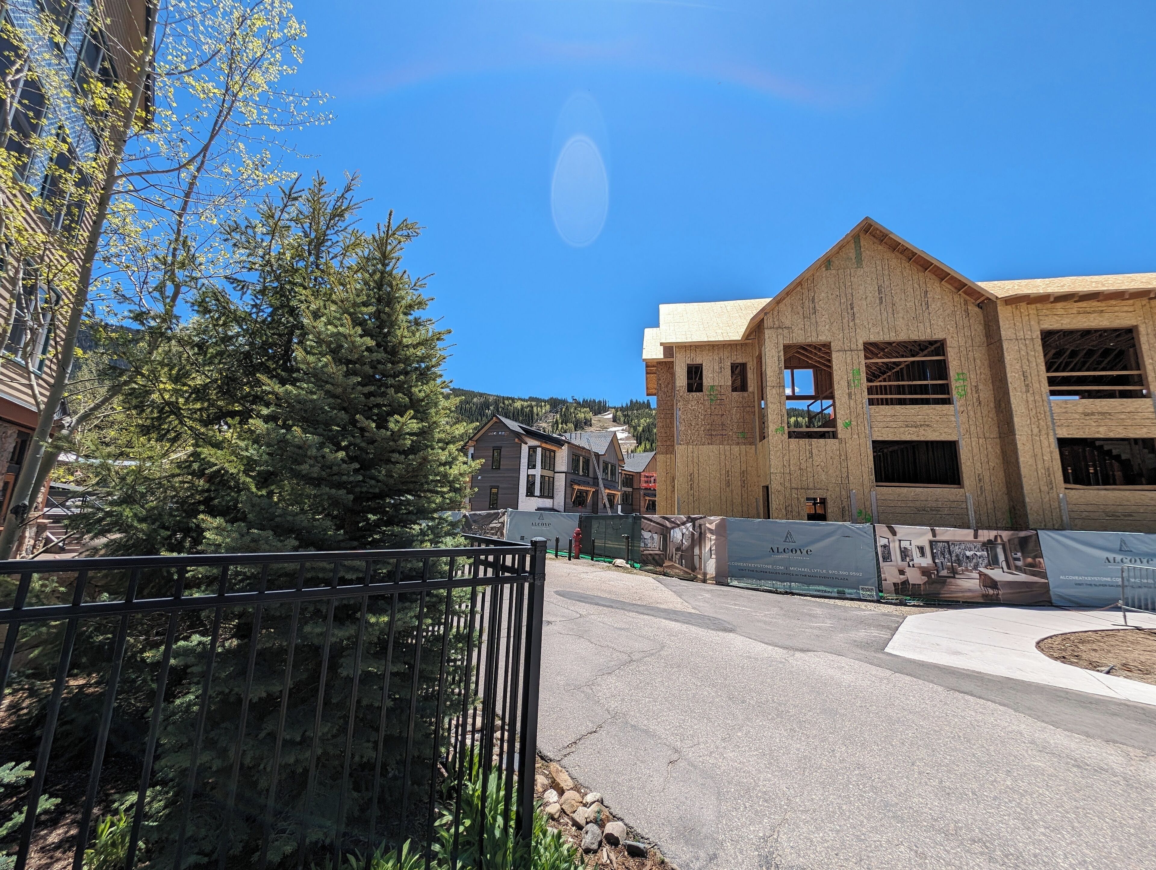 Un bâtiment en construction, doté d’une façade en bois, entouré d’arbres et bordé d’une zone pavée.