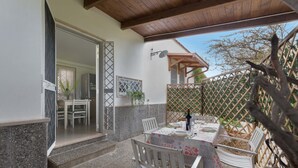 An outdoor patio with a table set for dining, surrounded by white chairs, and a wooden pergola overhead.