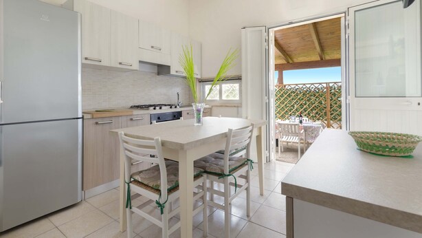 A modern kitchen with white cabinets, a stainless steel refrigerator, and a dining area with a table and chairs.