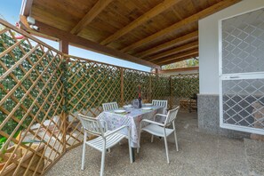 Eine Außenpatio mit einer Holz-Pergola, einem Tisch mit weißen Stühlen und einem Gitterzaun im Hintergrund.