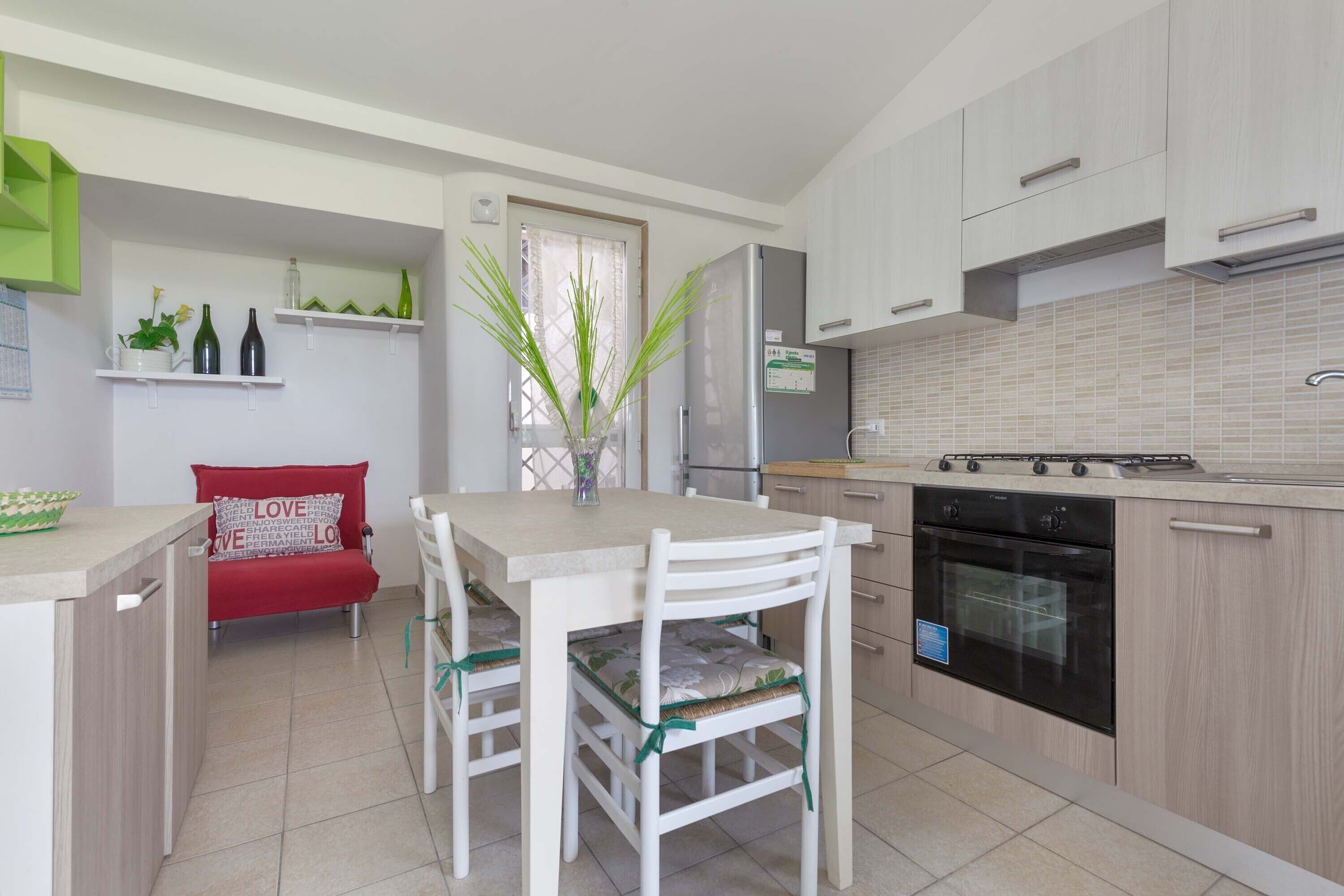 A compact kitchen with a dining area, a refrigerator, an oven, and a small seating area with a red chair.