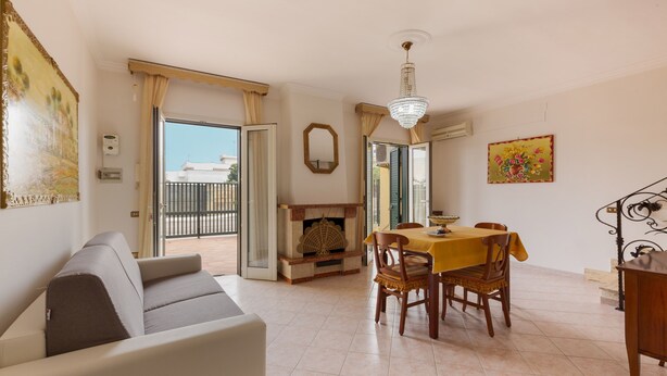 A living room with a sofa, dining table with chairs, a chandelier, and a fireplace. - 2348 Villino Mareluce by Barbarhouse (Porto Cesareo)
