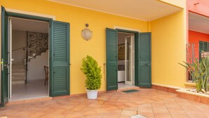 A yellow building with green shutters, a potted plant, and a tiled patio. - 2348 Villino Mareluce by Barbarhouse (Porto Cesareo)