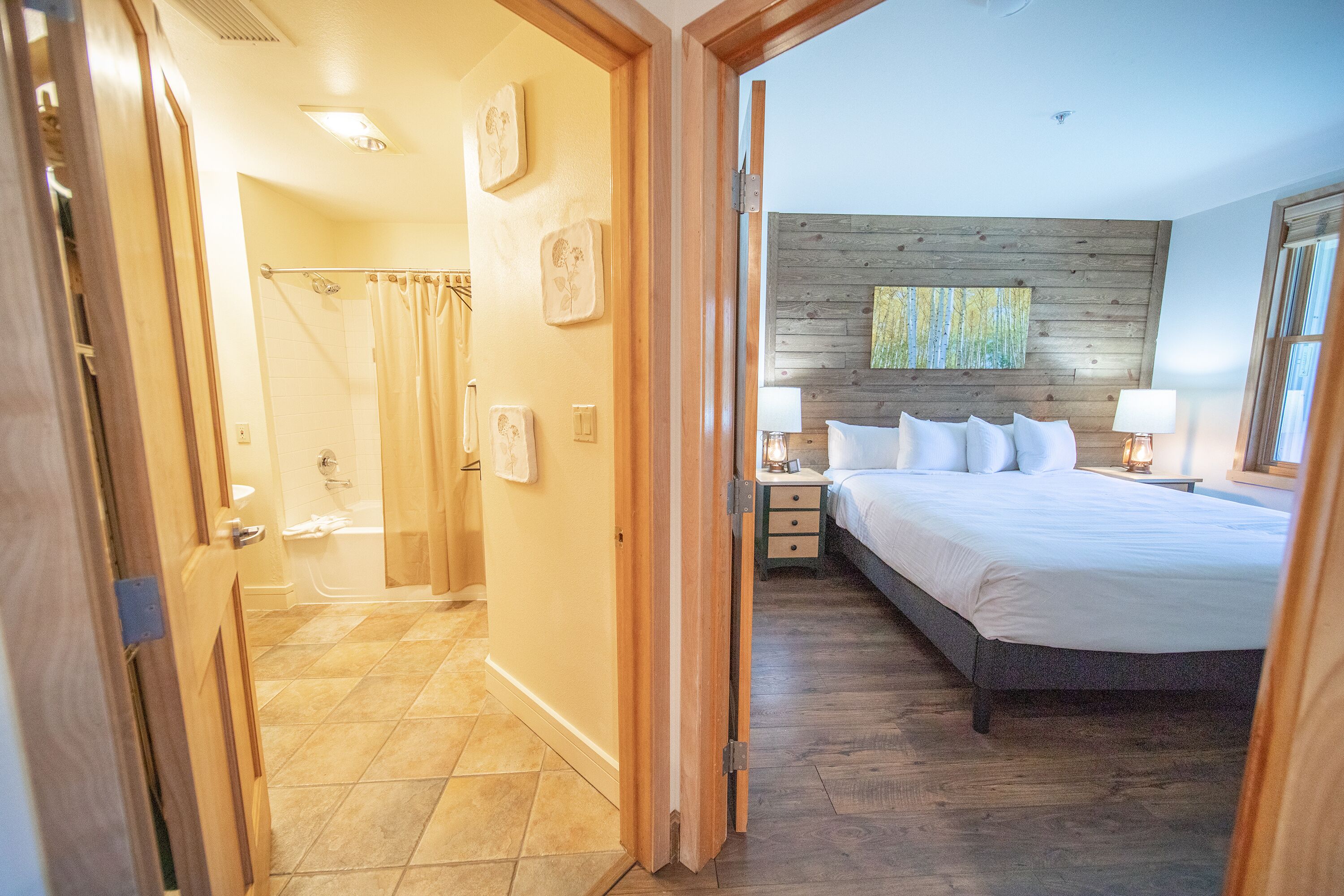 A bedroom with a wooden headboard, a bed with white bedding, a nightstand with a lamp, and a painting on the wall.