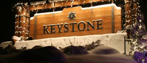 Une enseigne en bois portant le mot « KEYSTONE », illuminée par des lumières, et entourée de neige et de décorations festives.