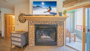 Una sala de estar con chimenea, un televisor montado encima y un reloj en la pared.