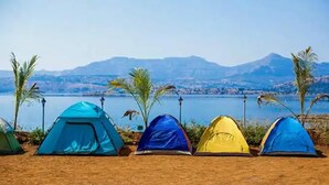 Une rangée de tentes colorées est installée sur une plage de sable, avec un lac et des montagnes en arrière-plan.