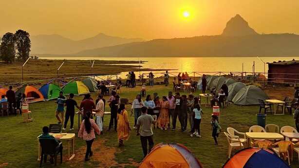 Un terrain de camping avec des tentes et des tables installées près d’une étendue d’eau, avec des montagnes en arrière-plan.