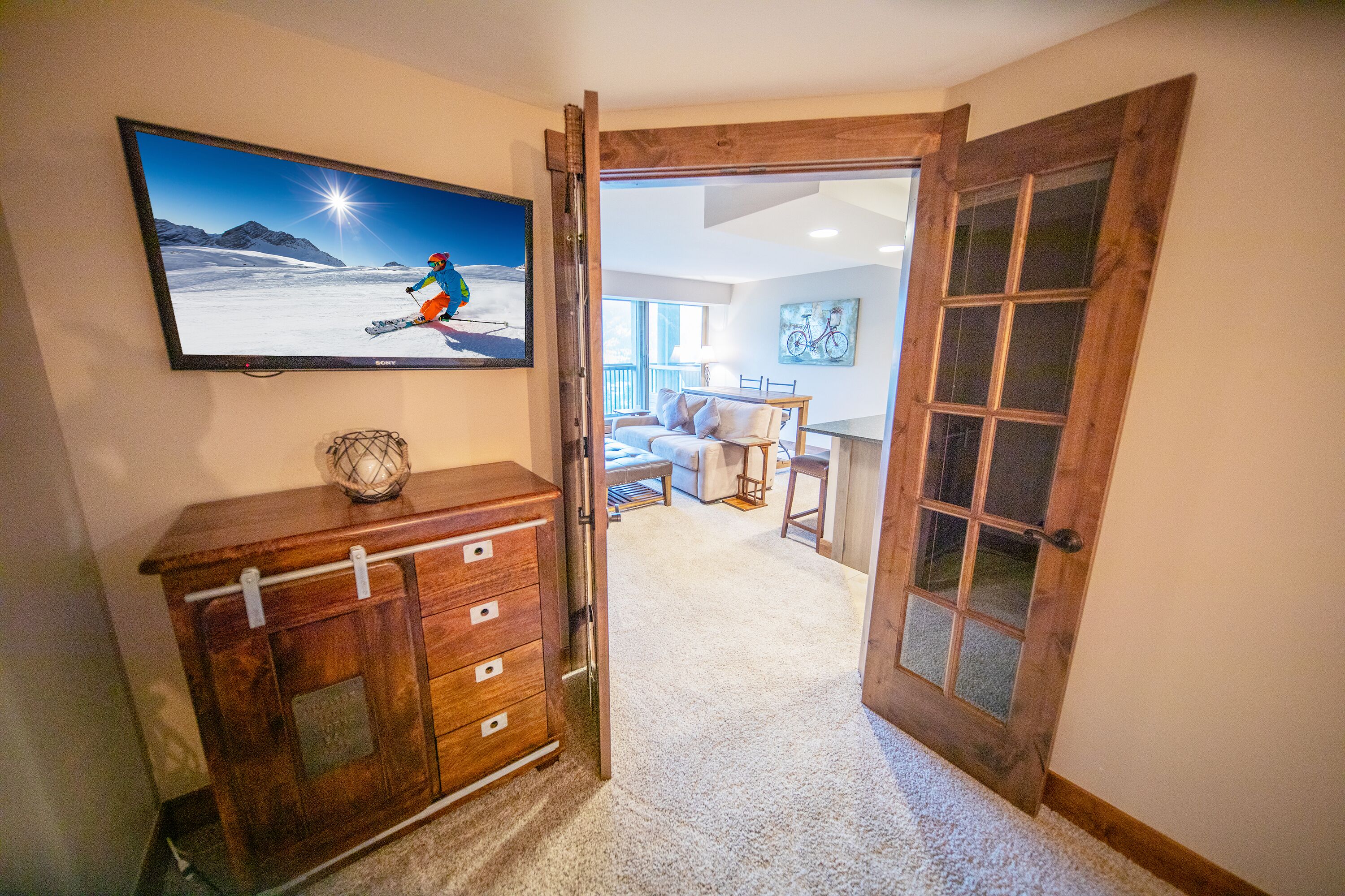 A room with a wooden dresser, a television displaying a skier, and a door leading to another room.