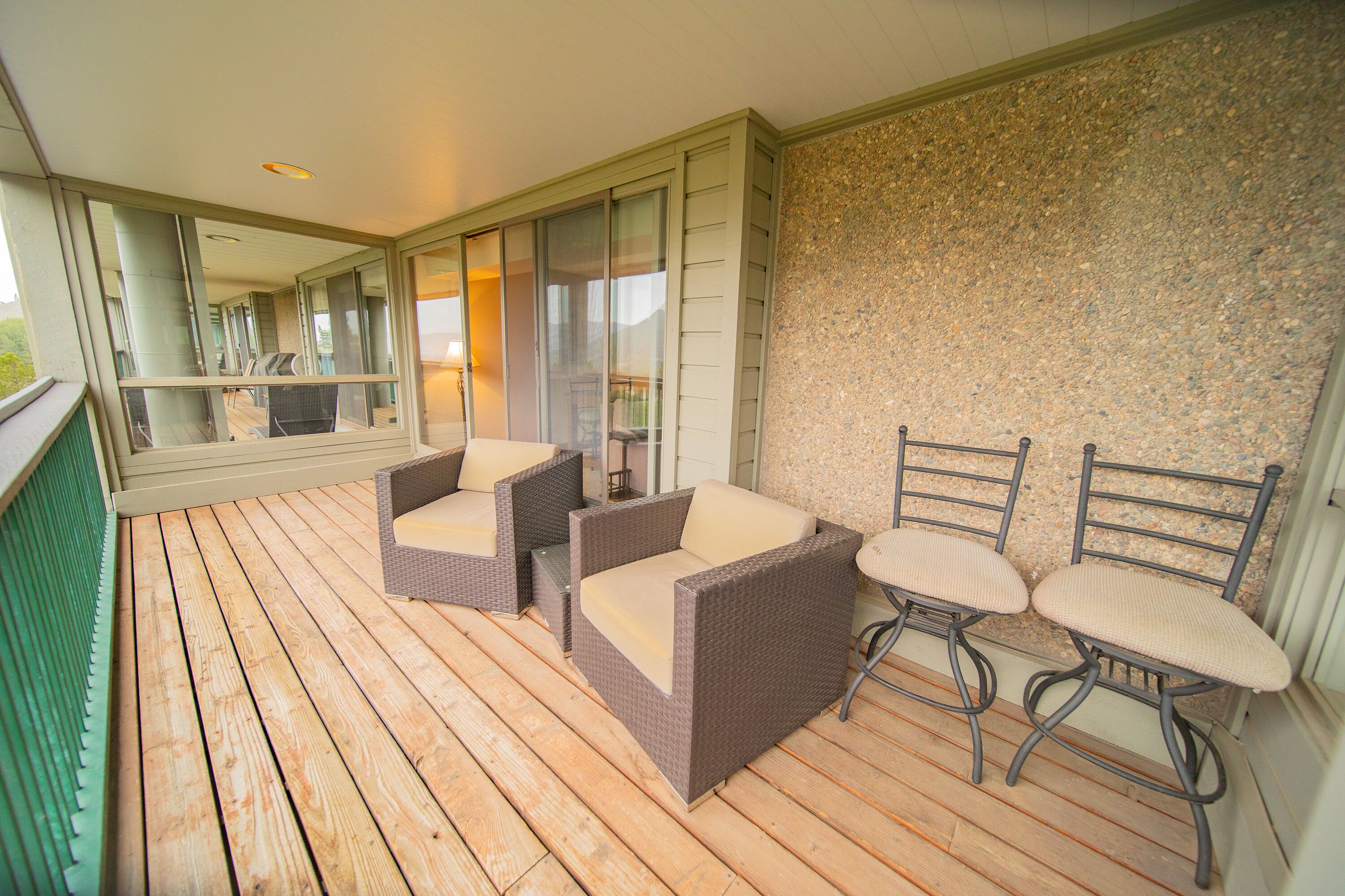 A wooden deck with wicker furniture and a stone wall.