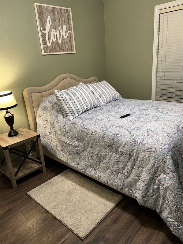 A bedroom with a bed, a bedside table with a lamp, a rug, and a wall with a 'love' sign. - Lovely and Comfy 3 bedrooms townhouse/chateau elan area (Braselton)