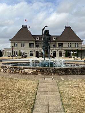A statue in front of a building with a fountain, a flag, and outdoor seating.