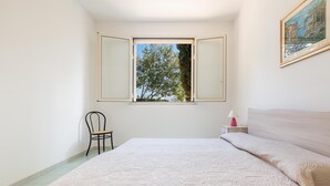 A bedroom with a bed, a chair, a nightstand, a lamp, and a window with an open shutter. - 2762 Zeus Apartments - Appartamento by Barbarhouse (Porto Cesareo)