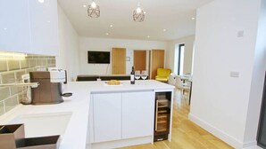 A modern kitchen with a central island, wooden flooring, and pendant lighting.