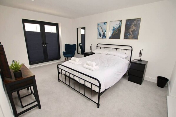 A modern bedroom with a large bed, a desk, a chair, a dresser, and a window with blinds. - Beachfront Walks With Sea View Balcony Deck (Worthing)