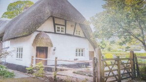 Een traditioneel rieten huis met een witte gevel, een houten poort en een tuin met een omheining.