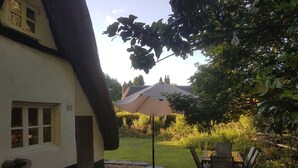 Een terras met een tafel en stoelen, een hangende lamp en een gebouw met rieten dak op de achtergrond.