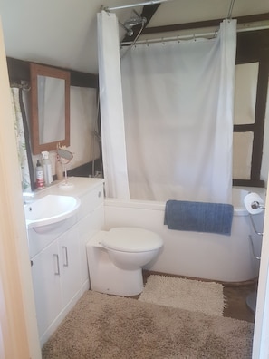 A bathroom with a white sink, toilet, and shower curtain. There is a mirror above the sink and a towel rack next to the toilet.