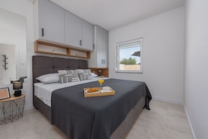 A modern bedroom with a large bed, a bedside table with a lamp, a window with a view, and built-in storage cabinets.
